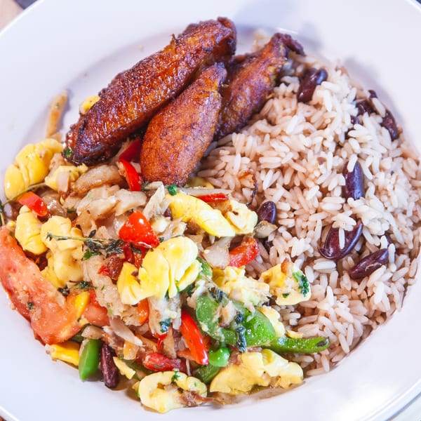 A white plate with Jamaican ackee and saltfish, rice and peas, and fried plantains.