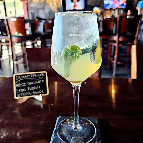 A refreshing cocktail with mint and lime, next to a dessert special sign, in a restaurant.
