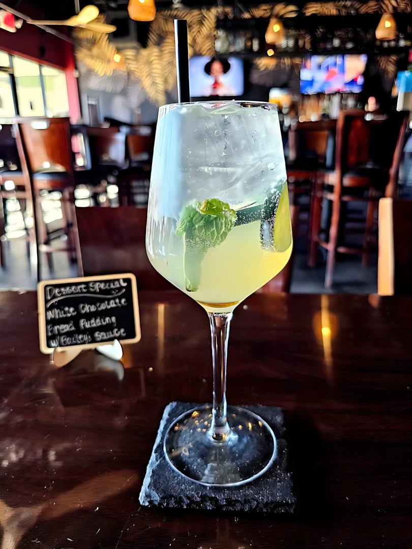 A refreshing cocktail with mint and lime, next to a dessert special sign, in a restaurant.