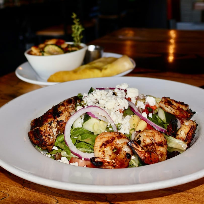 Grilled chicken and shrimp salad with feta, red onion, and cucumber, with a side of bread.