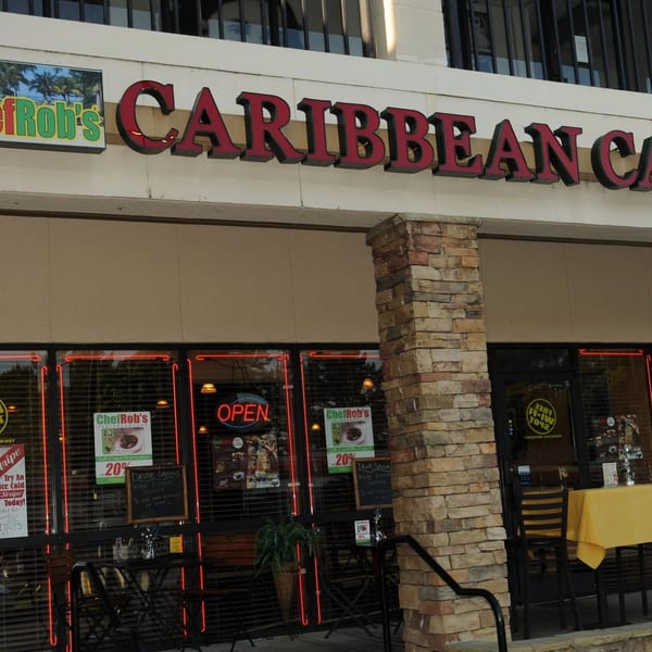 Chef Rob's Caribbean Cafe storefront with an "OPEN" sign, outdoor seating, and promotional posters.