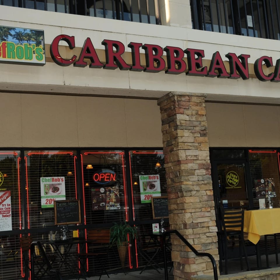 Chef Rob's Caribbean Cafe storefront with an "OPEN" sign, outdoor seating, and promotional posters.