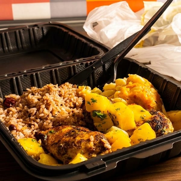 Takeout container with rice, chicken, and yellow potatoes, with a plastic fork and bag.