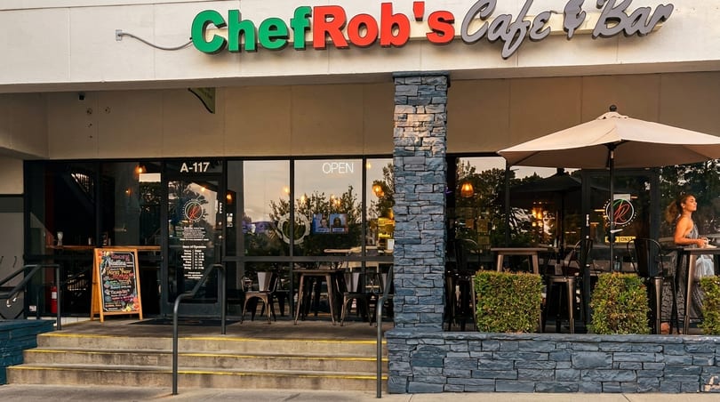 Exterior of Chef Rob's Cafe & Bar with outdoor seating, a menu board, and a woman.