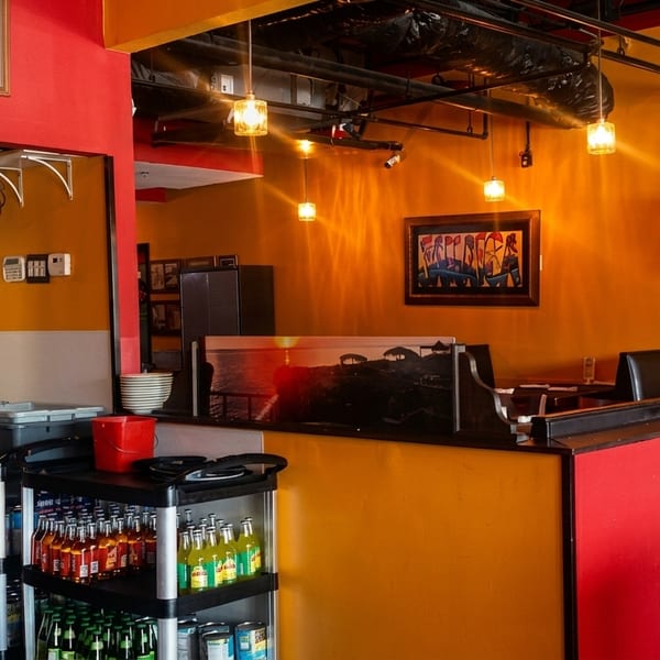 Restaurant interior with orange and red walls, a counter with drinks, and dining tables with a TV.