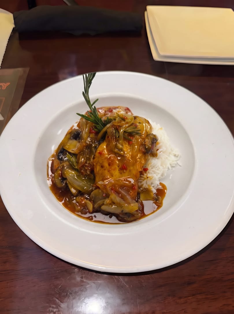 Chicken with mushrooms and onions in a rich sauce, served over white rice on a white plate.