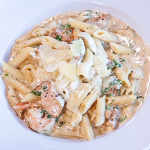Penne pasta with shrimp, creamy sauce, and shaved Parmesan cheese in a white bowl.