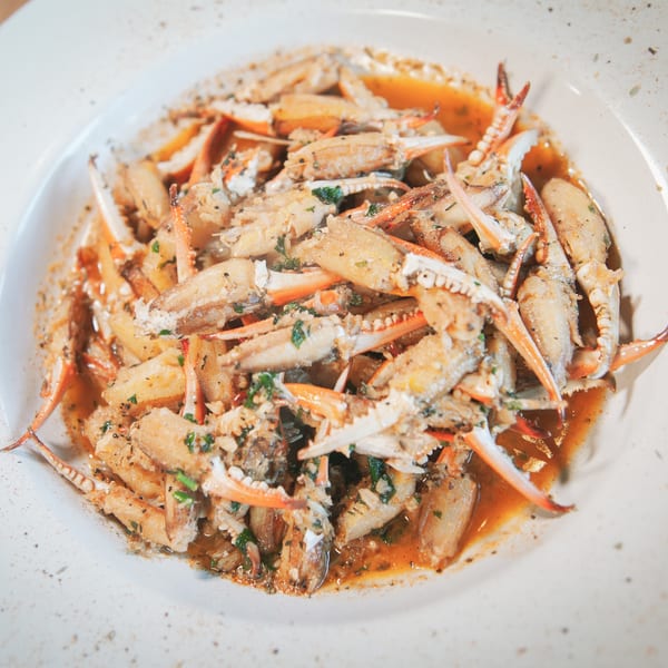A white bowl filled with crab claws and pieces in a savory sauce, garnished with herbs.