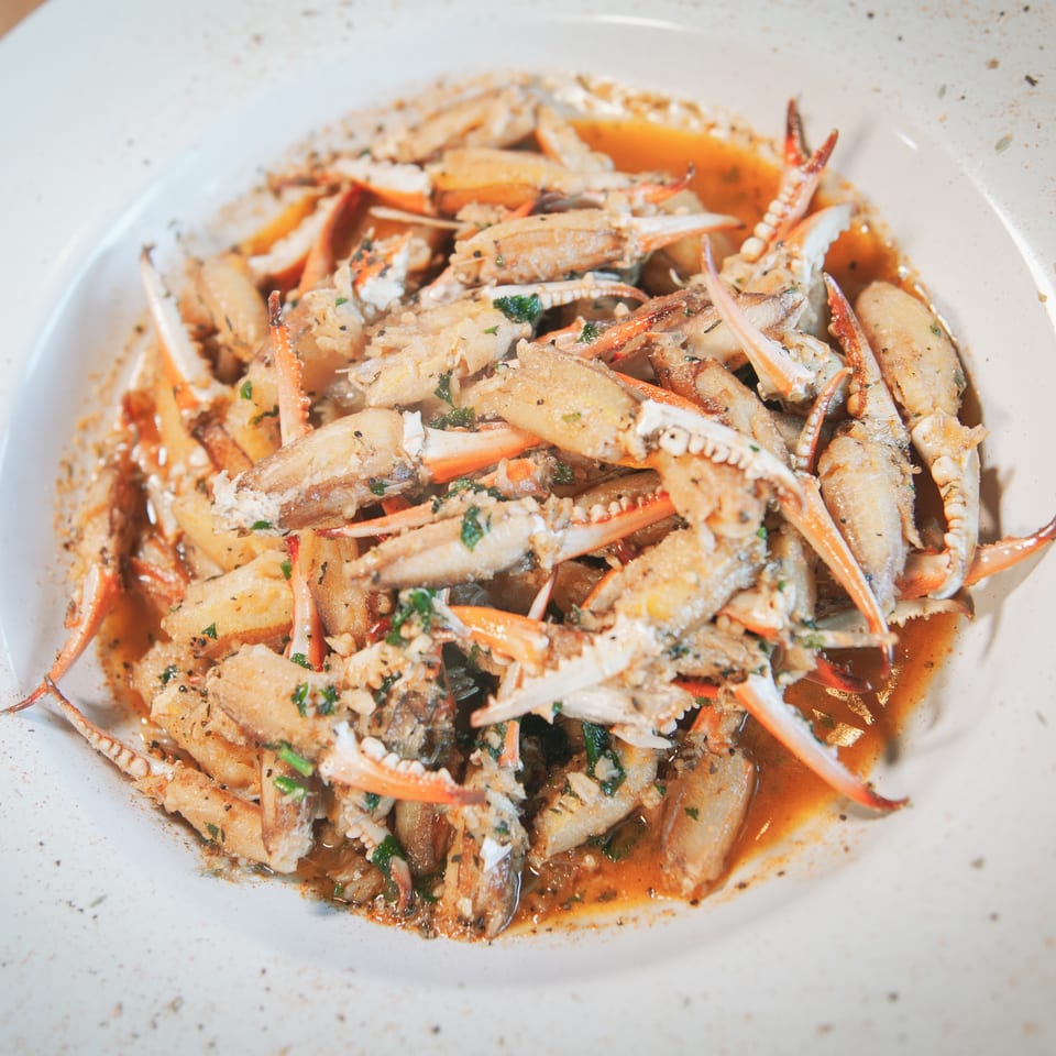 A white bowl filled with crab claws and pieces in a savory sauce, garnished with herbs.
