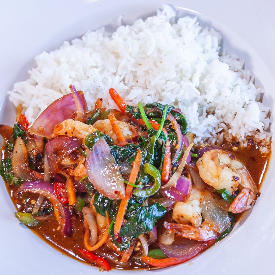 Shrimp stir-fry with red onions, carrots, and green peppers, served with white rice.
