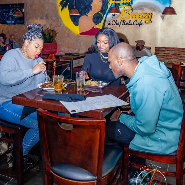 Three people dining at a table in a restaurant with a colorful mural on the wall.