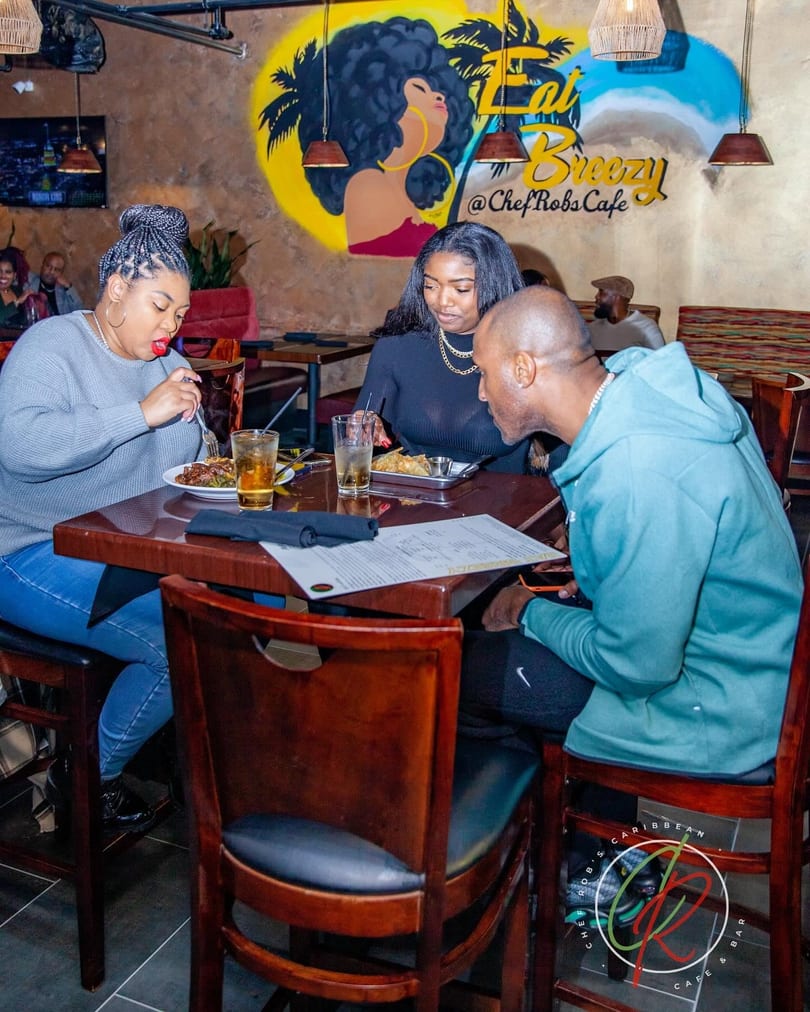 Three people dining at a table in a restaurant with a colorful mural on the wall.