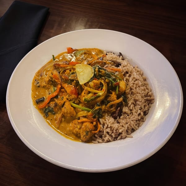 Curry chicken with vegetables and brown rice on a white plate, with a black napkin on a wooden table.